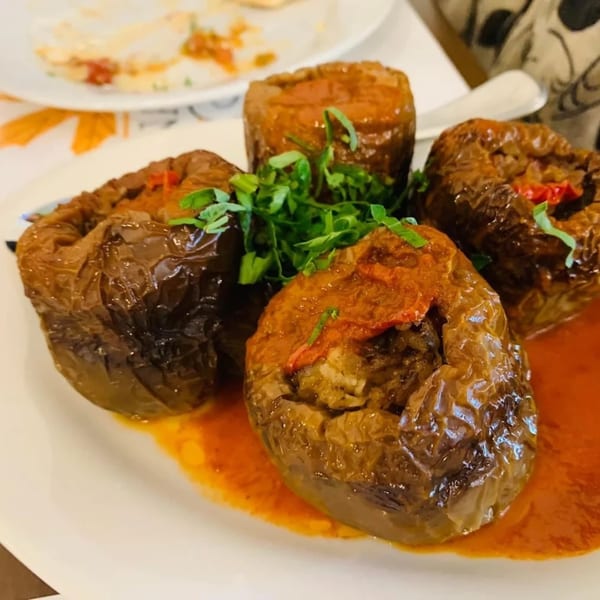Four stuffed bell peppers, topped with tomato and parsley, in a rich red sauce on a white plate.