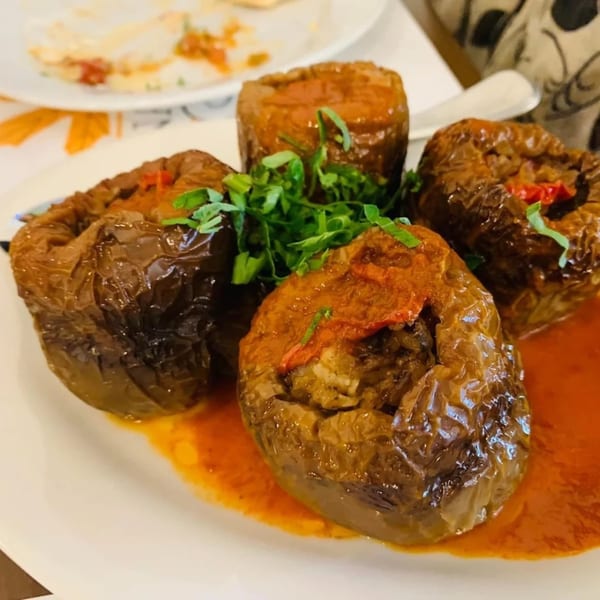 Four stuffed bell peppers in tomato sauce, garnished with fresh parsley on a white plate.