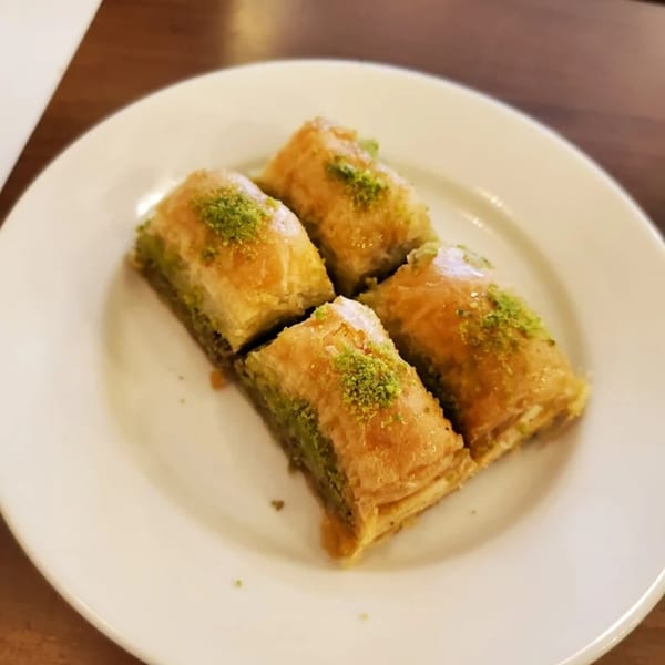 Four pieces of golden-brown baklava with green pistachio sprinkles on a white plate.