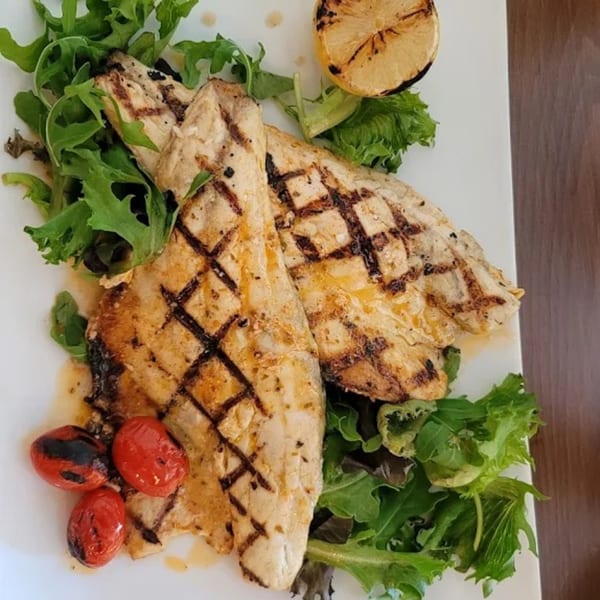 Grilled fish fillets with char marks, served on a bed of greens with roasted tomatoes and lemon.