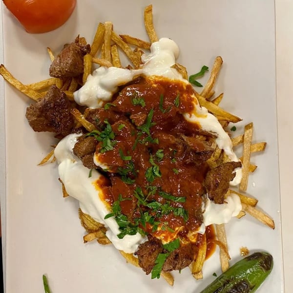 Cinar Restaurant's Mediterranean dish with fries, meat, yogurt, red sauce, and parsley.